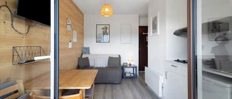 Um interior moderno com área de refeições de madeira, sofá, mesa pequena com abajur e cozinha com fogão.