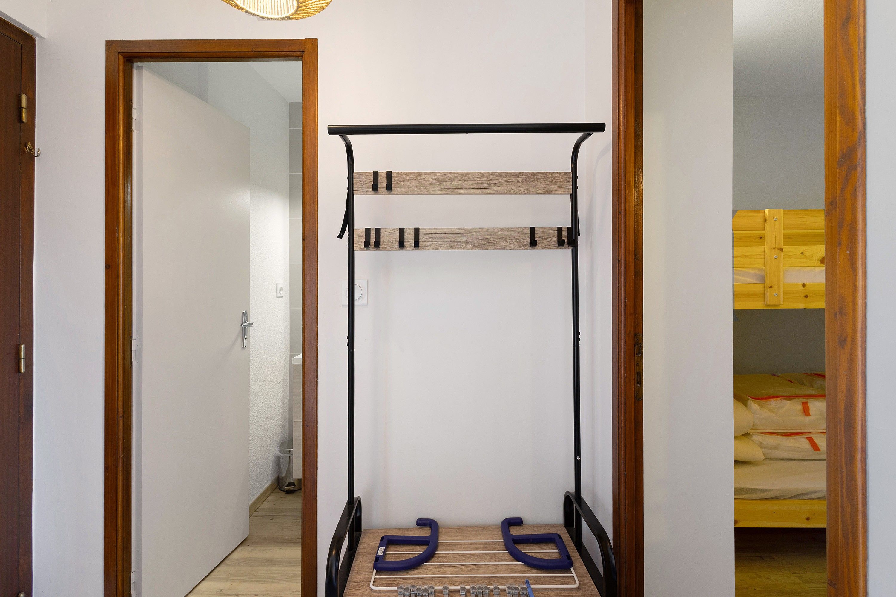 Un pasillo estrecho con un perchero metálico y una cama con ropa de cama amarilla.