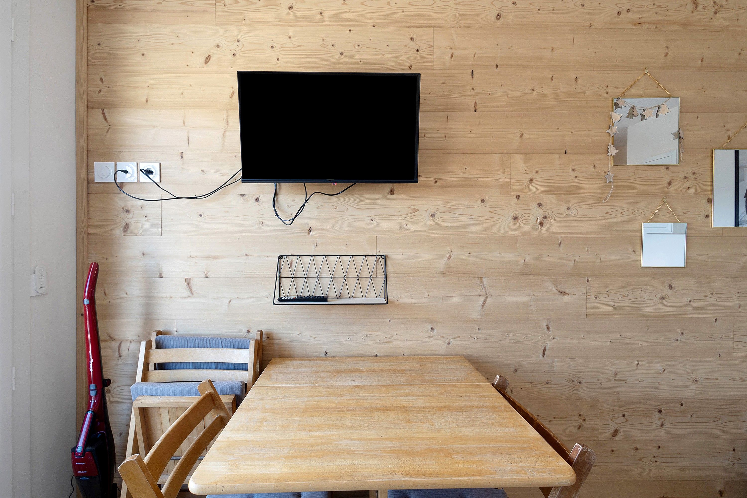 Habitación con pared de madera, televisor montado, teclado, mesa y sillas.