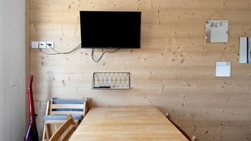 Habitación con pared de madera, televisor montado, teclado, mesa y sillas.