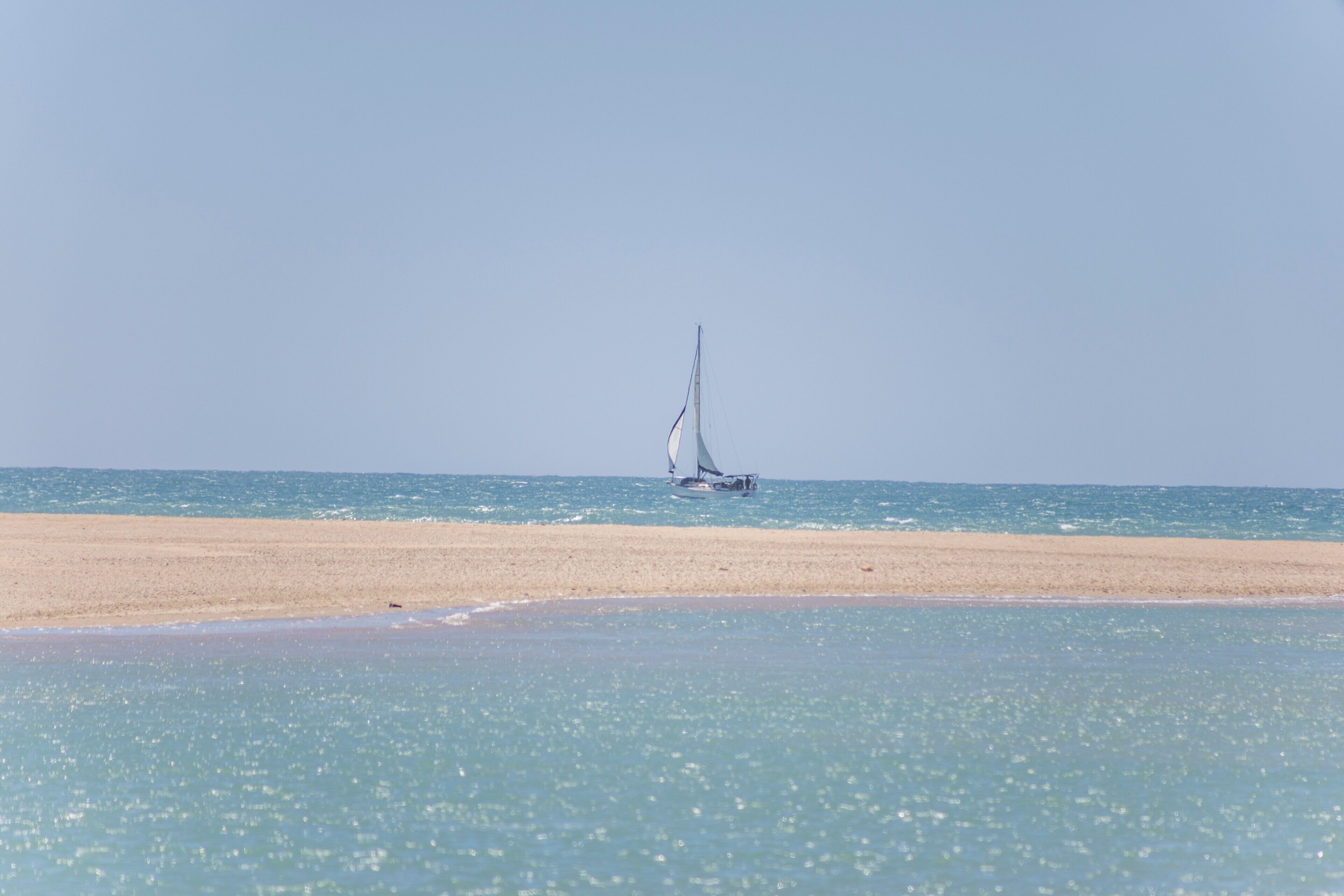 Une plage avec un voilier à l’horizon.