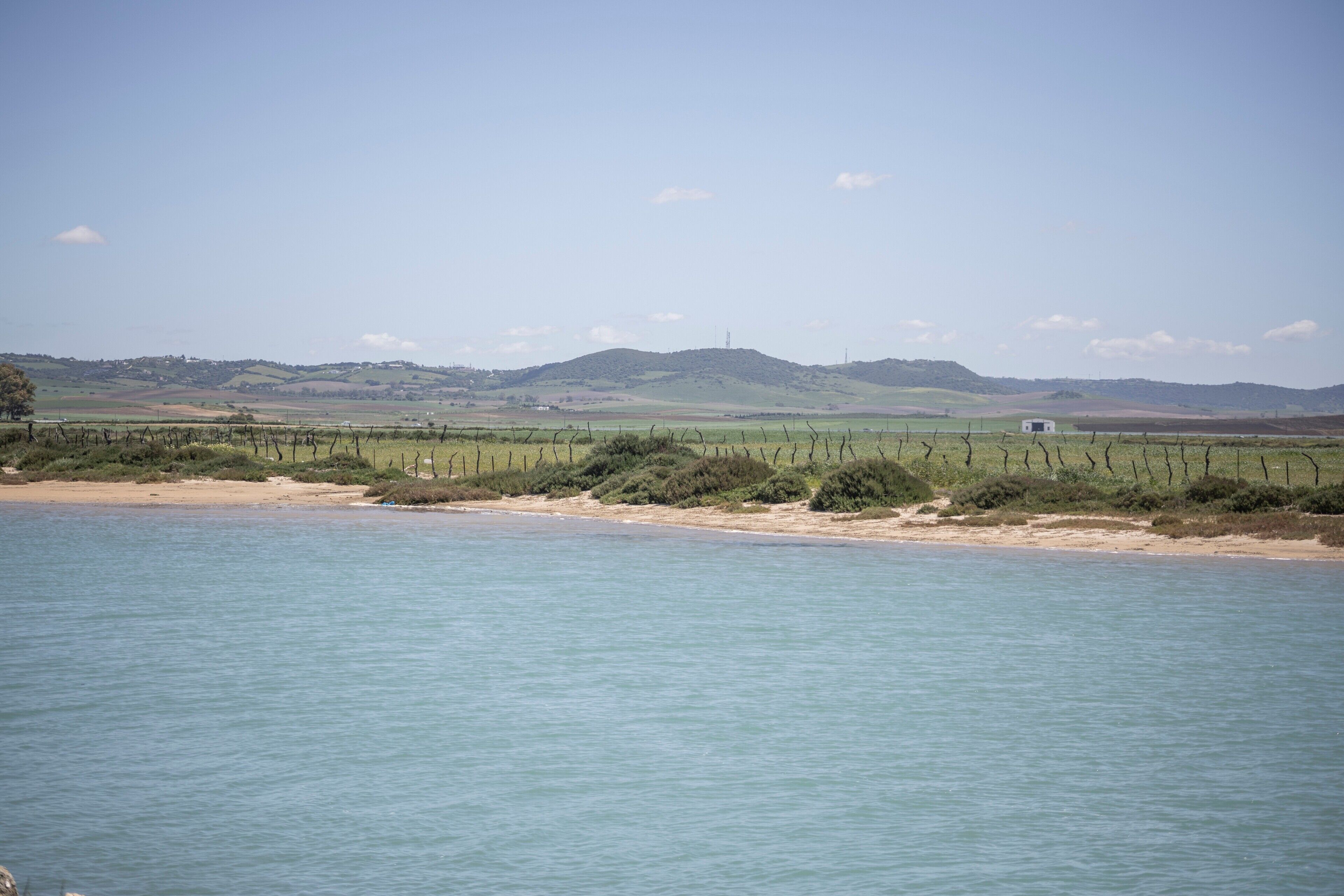 Un paysage côtier avec un ciel dégagé, une mer calme et des collines à l’horizon.