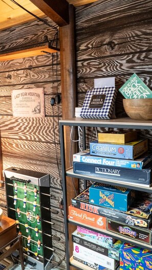 Puinen seinä, jossa on kyltti, jossa lukee: ”Lazy Bear Mountain -leirintäalue”, ja teline, jossa on lautapelejä, kuten ”Cranium”, ”Connect Four” ja ”Risk”.
