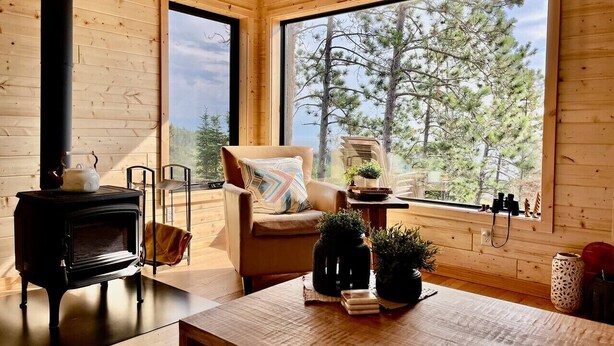 Ein gemütliches Blockhaus mit Holzausstattung, einer Couch, einem Tisch mit Pflanzen und einem großen Fenster mit Blick auf den Wald.