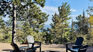 Ein Campingplatz mit Adirondack-Stühlen, einer Feuerstelle und Blick auf Kiefern.