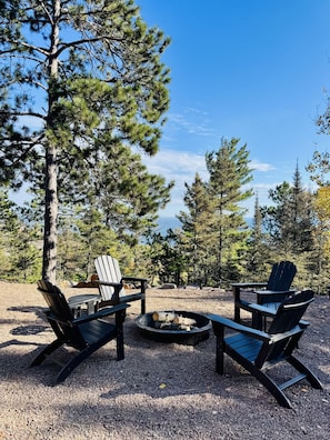 Ein Campingplatz mit Adirondack-Stühlen, einer Feuerstelle und Blick auf Kiefern.