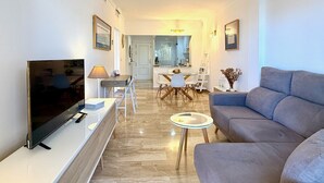 En moderne stue med et fladskærms-tv, en sofa, et sofabord og et spiseområde med bord og stole.