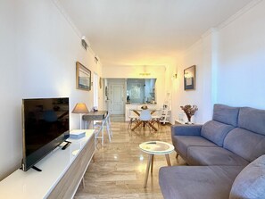 Ein modernes Wohnzimmer mit Flachbildfernseher, einer Couch, einem Couchtisch und einem Essbereich mit Tisch und Stühlen.