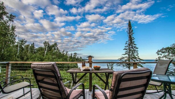 A deck with chairs and a table, overlooking a body of water and trees.