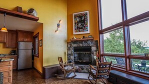 A kitchen with wooden cabinets, a stone fireplace, and a large window overlooking greenery.