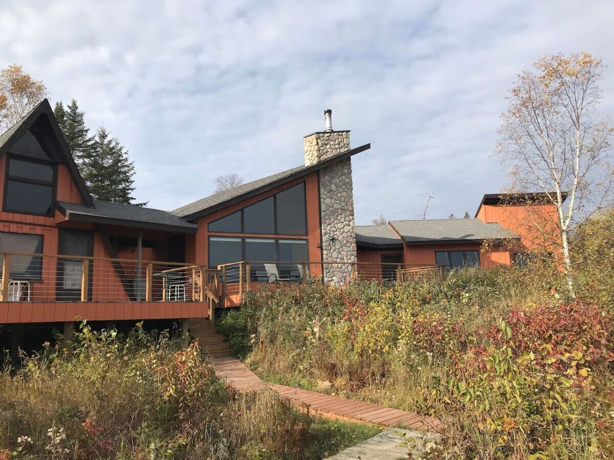 A modern house with a stone chimney, large windows, and a wooden deck.