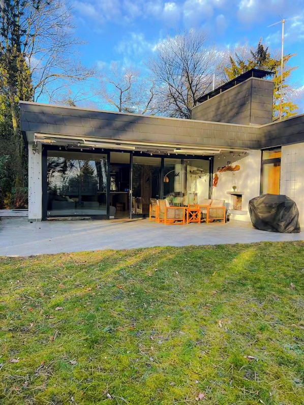 Une maison moderne dotée d’une grande porte vitrée, d’un espace salon extérieur et d’une cheminée en pierre.