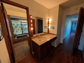 A bathroom with a large mirror, vanity, and a window with a view of a balcony.