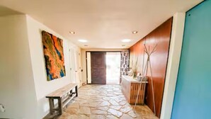 A hallway with a stone floor, a bench, a wooden door, and a wall with a colorful abstract painting. - Guest Wing at Dairy Goat Farm (Somis)
