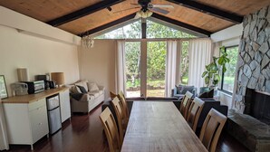 A spacious dining area with a wooden table and chairs, a kitchen with a refrigerator and coffee maker, and a stone fireplace. - Guest Wing at Dairy Goat Farm (Somis)