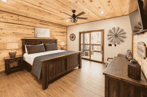 A bedroom with a wooden ceiling, a bed with a headboard, a nightstand, a desk, and a window with a view.
