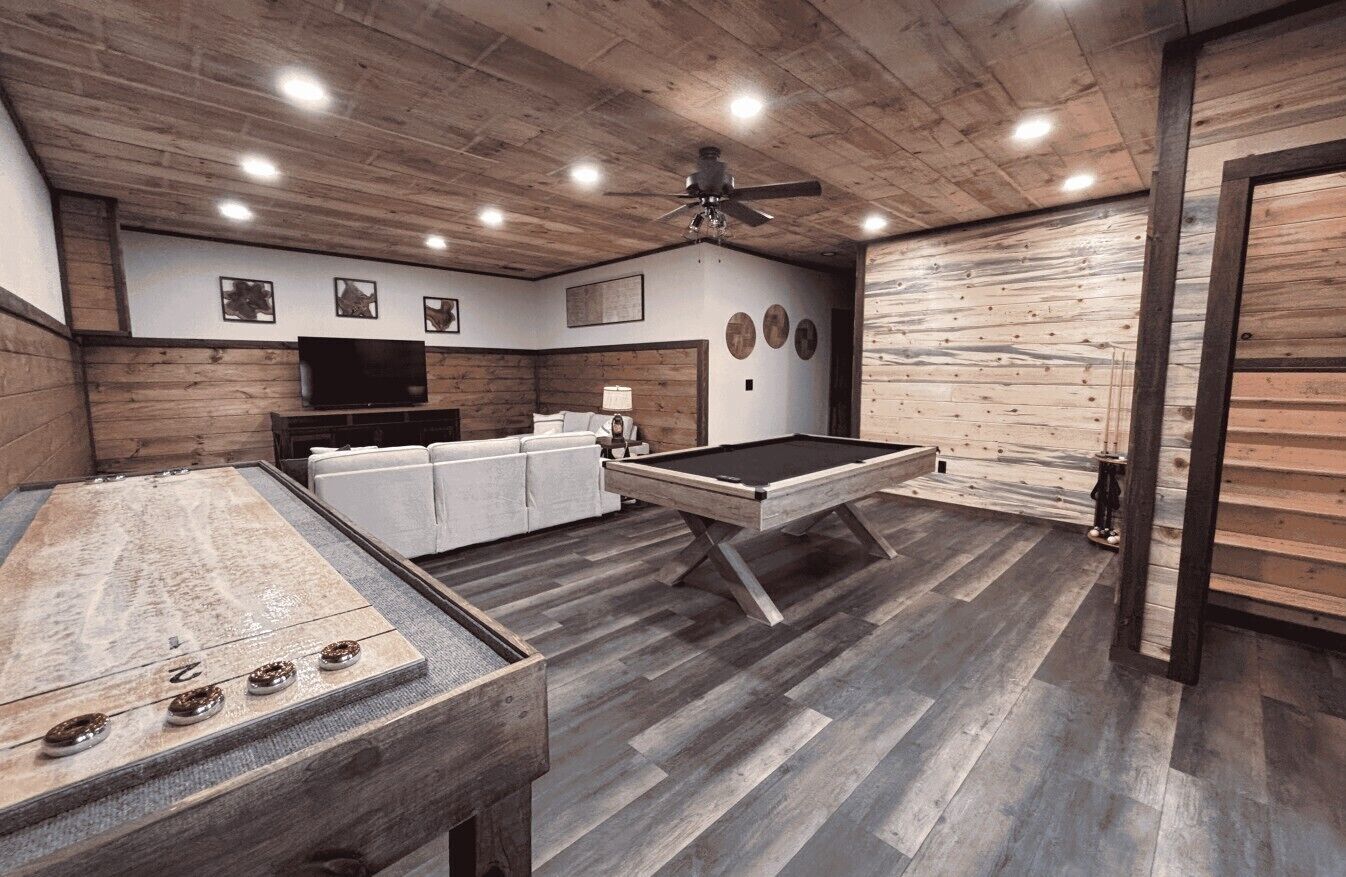 A room with a pool table, a sofa, a television, and a ceiling fan.
