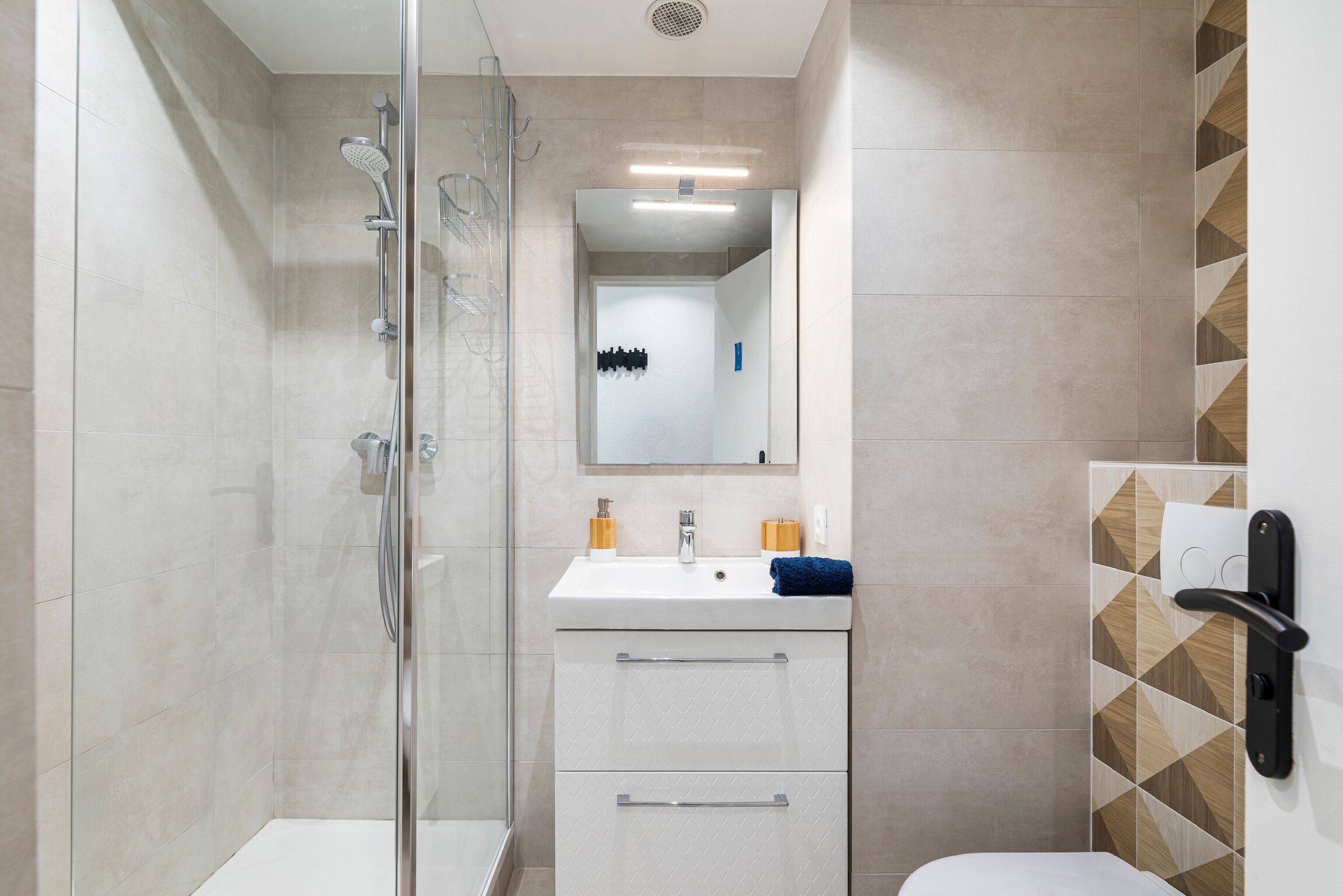 Un baño moderno con cabina de ducha de vidrio, un lavamanos blanco con espejo y un inodoro.