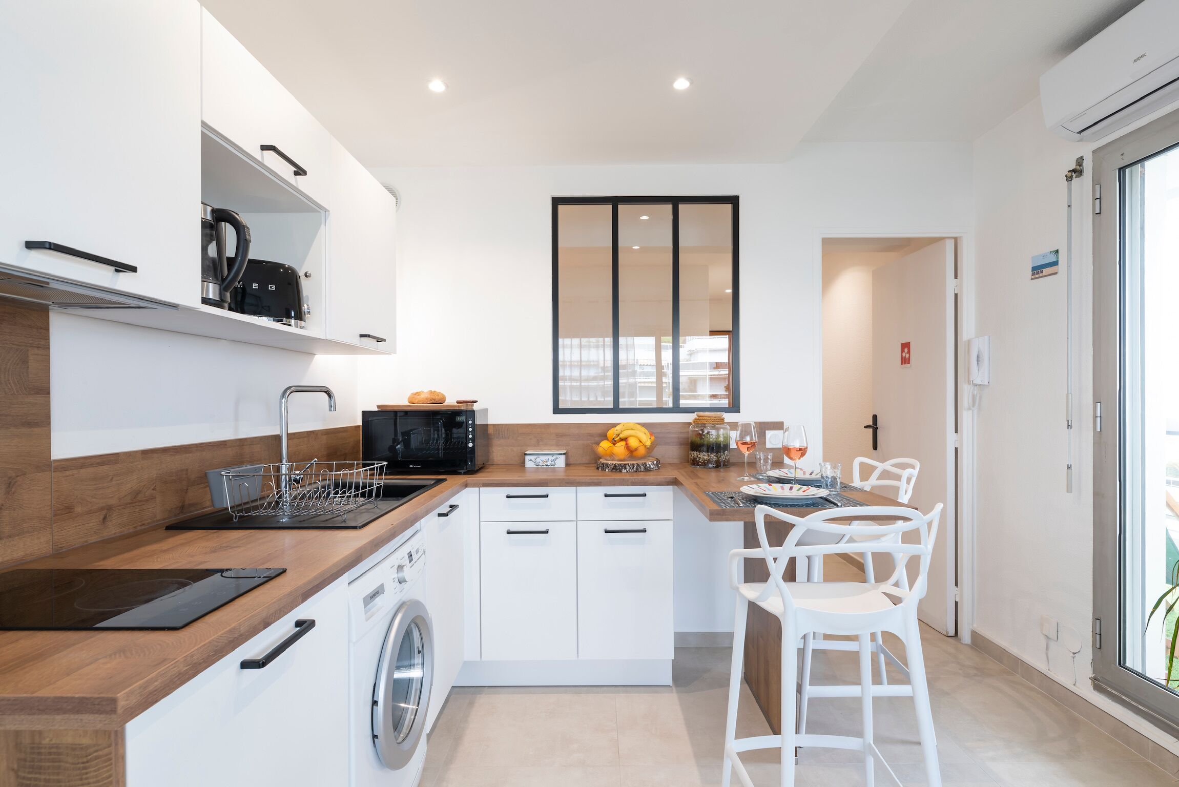 A modern kitchen with a dishwasher, microwave, and a sink. There is a dining area with white chairs and a table.