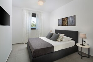 A modern bedroom with a bed, a bedside table, a lamp, a TV, and a window with curtains. - Vivi Rent Fažana - Villa Fasana Apartment 1 (Fažana)