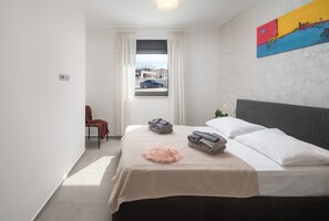 Ein Hotelzimmer mit Bett, Sessel, Fenster mit Blick auf Gebäude und einem Gemälde an der Wand.