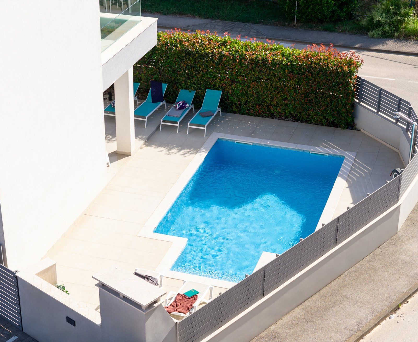Una piscina rettangolare con bordo piastrellato, circondata da sdraio e un siepe.