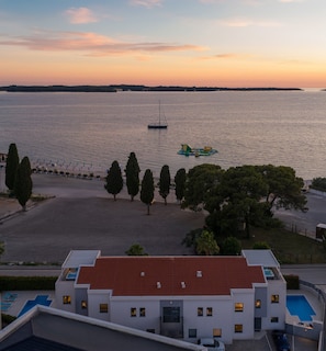 Ein modernes Gebäude mit rotem Ziegeldach, einem Schwimmbad und Blick auf ein ruhiges Gewässer mit Segelboot und Wasserspielplatz.