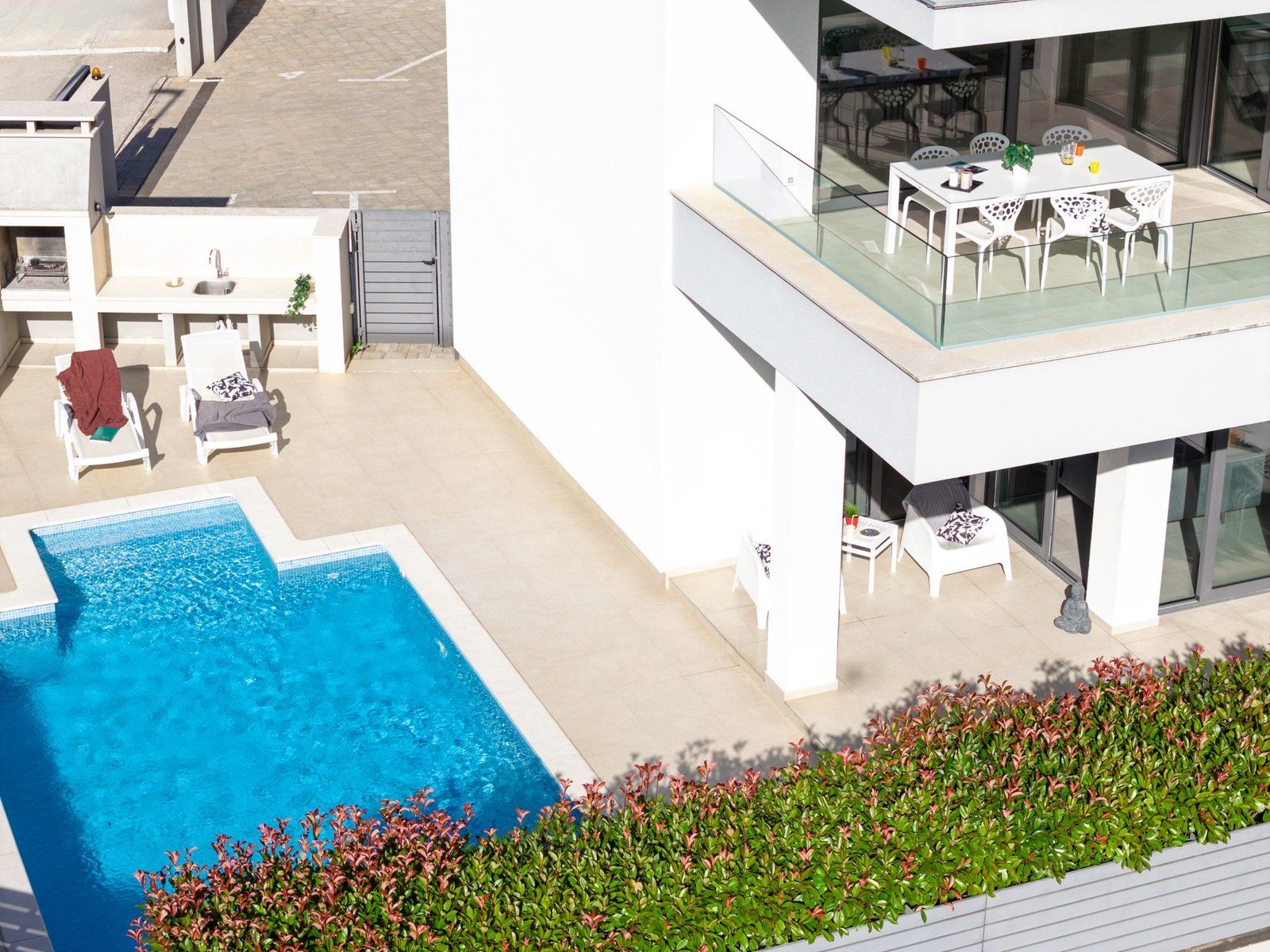 Un espace piscine extérieur moderne, doté d’une balustrade en verre, de chaises longues et d’une table à manger avec des chaises.
