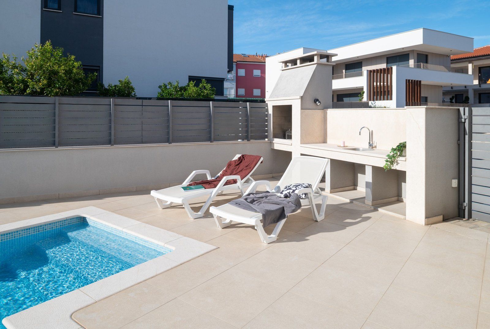 A rooftop pool area with lounge chairs and a small kitchen area.