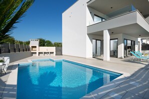 A modern poolside area with a clear blue pool, a white building with a balcony, and a small structure in the background. - Vivi Rent Fažana - Villa Fasana Apartment 1 (Fažana)