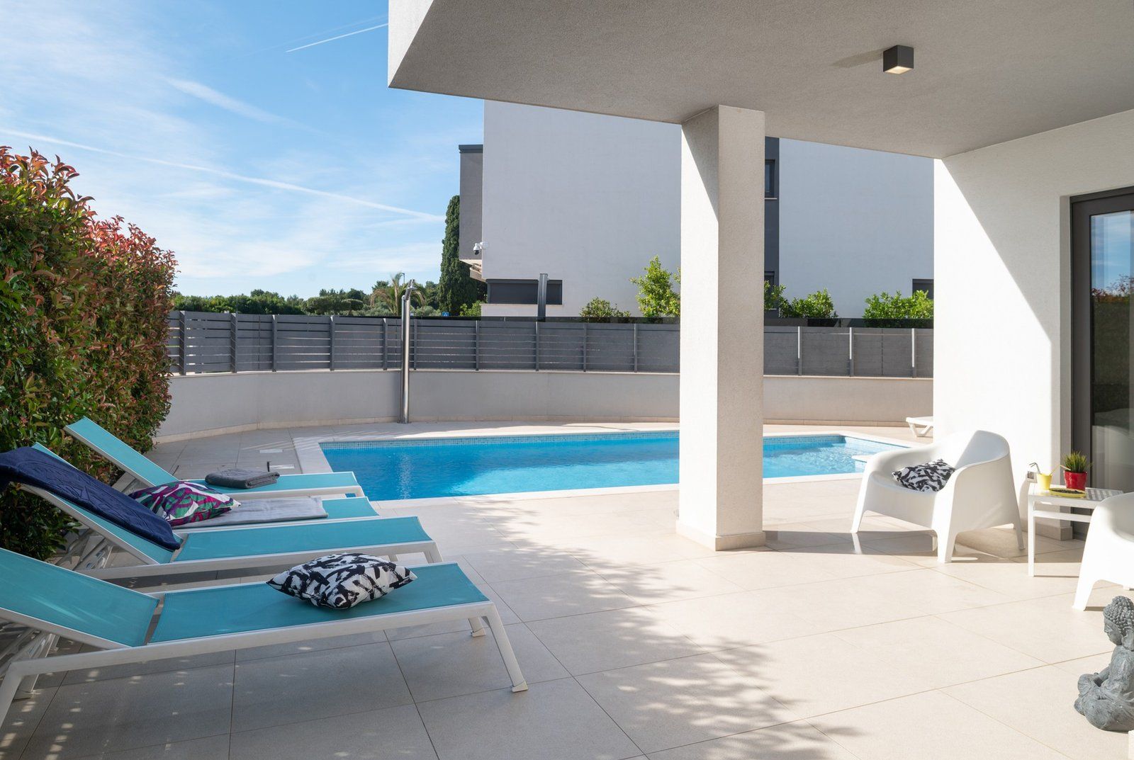 A rooftop pool area with lounge chairs and a small table, surrounded by a white building and greenery.