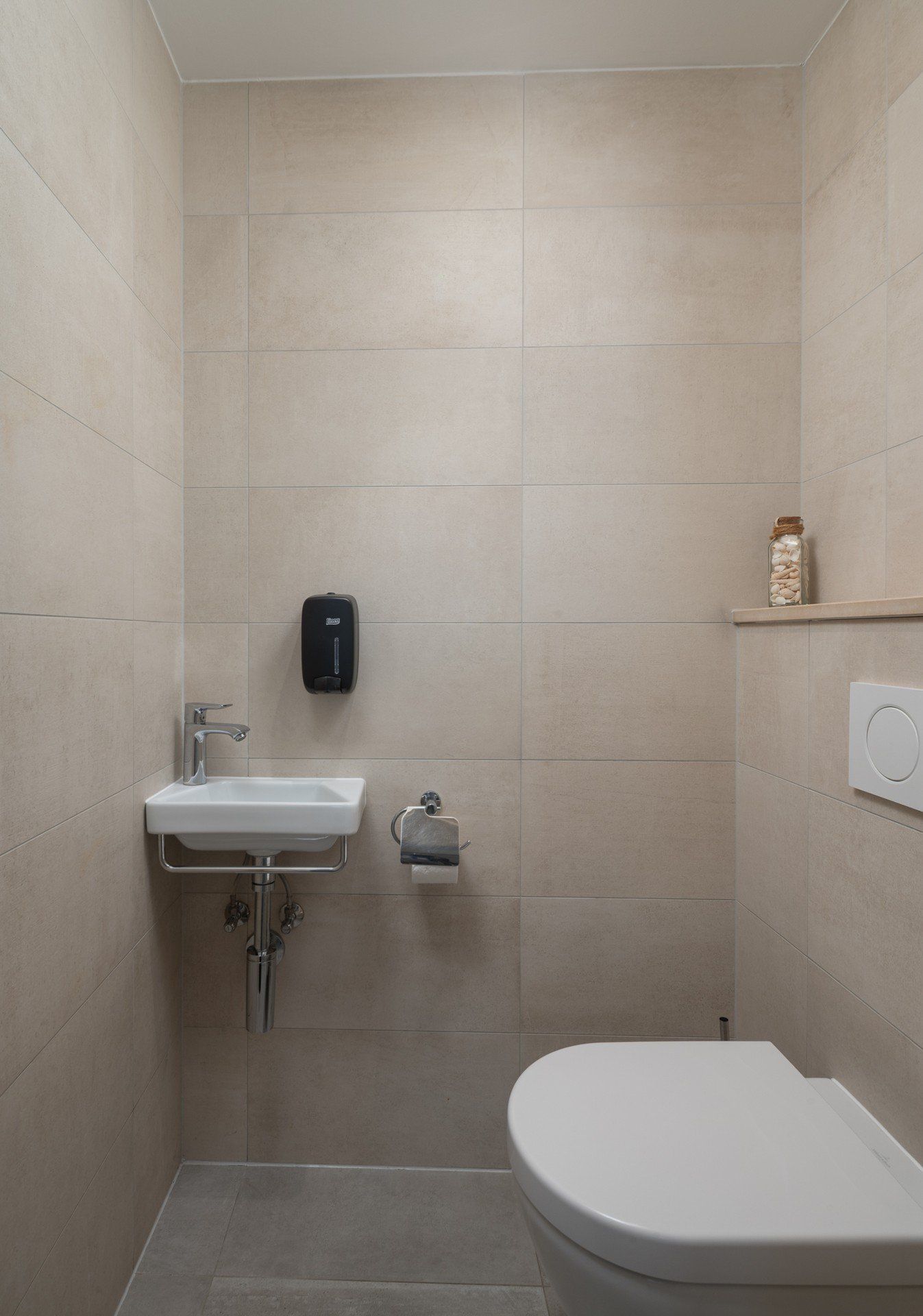 A small, modern bathroom with a toilet, sink, and hand dryer.