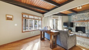 A spacious living area with a stone fireplace, wooden ceiling beams, and a large window.