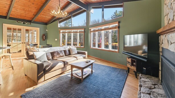 A spacious living room with a wooden ceiling, large windows, a sofa, a coffee table, and a fireplace.