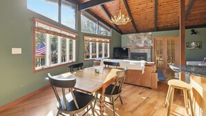 A spacious kitchen with a wooden ceiling, large windows, a stone fireplace, and a dining area with chairs and a table.