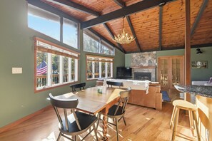 A spacious kitchen with a wooden ceiling, large windows, a stone fireplace, and a dining area with chairs and a table. - Gunstock Chalet - Close to Gunstock, BNH Pavilion Concerts, and Lake Winni (Gilford)