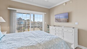 Una camera da letto con un letto, una cassettiera, una ventola a soffitto, una TV e vista su un quartiere residenziale.