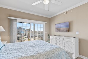 A bedroom with a bed, a dresser, a ceiling fan, a TV, and a view of a residential area. - Sea Bright 203 by Seaside Vacations & Sales (Ocean City)