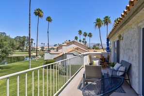 A balcony with wicker furniture, a view of a lake, and palm trees. - Desert Falls Fairway Retreat (Palm Desert)
