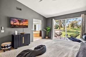 Une chambre moderne avec un grand lit, une télévision, une commode en bois foncé et un balcon donnant sur un terrain de golf.