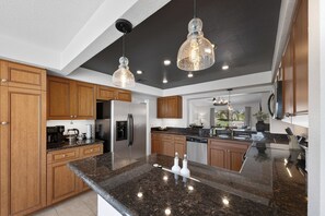 A modern kitchen with granite countertops, stainless steel appliances, wooden cabinets, and pendant lighting. - Desert Falls Fairway Retreat (Palm Desert)