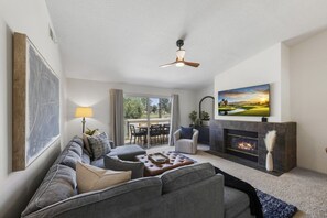 A living room with a sectional sofa, a fireplace, a television, and a view to the outside. - Desert Falls Fairway Retreat (Palm Desert)