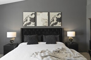 A bedroom with a tufted headboard, a large bed, two bedside tables with lamps, and three framed artworks on the wall. - Desert Falls Fairway Retreat (Palm Desert)