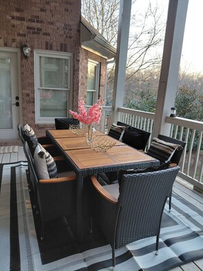 Une terrasse couverte avec une table en bois et des chaises en osier, un mur en briques et une vue sur les arbres.