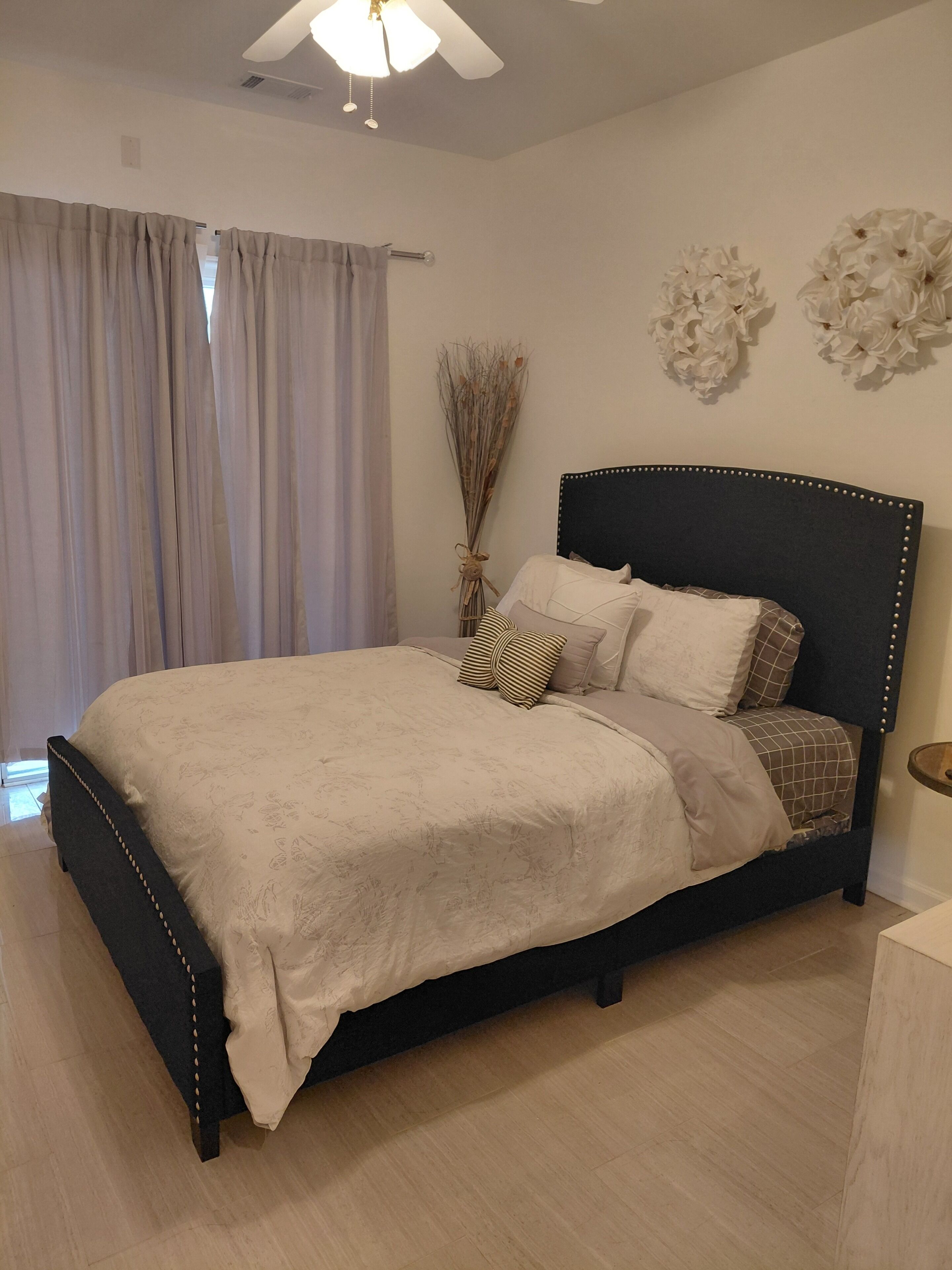 A bedroom with a bed, curtains, a ceiling fan, and wall decorations.