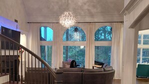 Un'ampia zona giorno con un'imponente scala, grandi finestre e un lampadario.