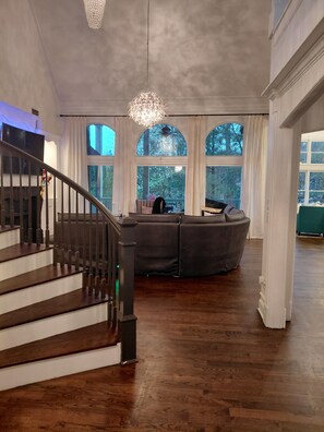 A spacious living area with a grand staircase, large windows, and a chandelier. - World Cup FIFA Multi Family Retreat Near Airport (Atlanta)