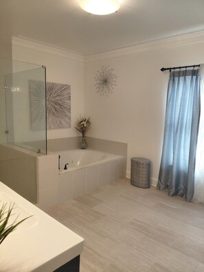 Une salle de bain moderne avec une douche à parois de verre, une baignoire sur pieds, un élément décoratif mural et un rideau.