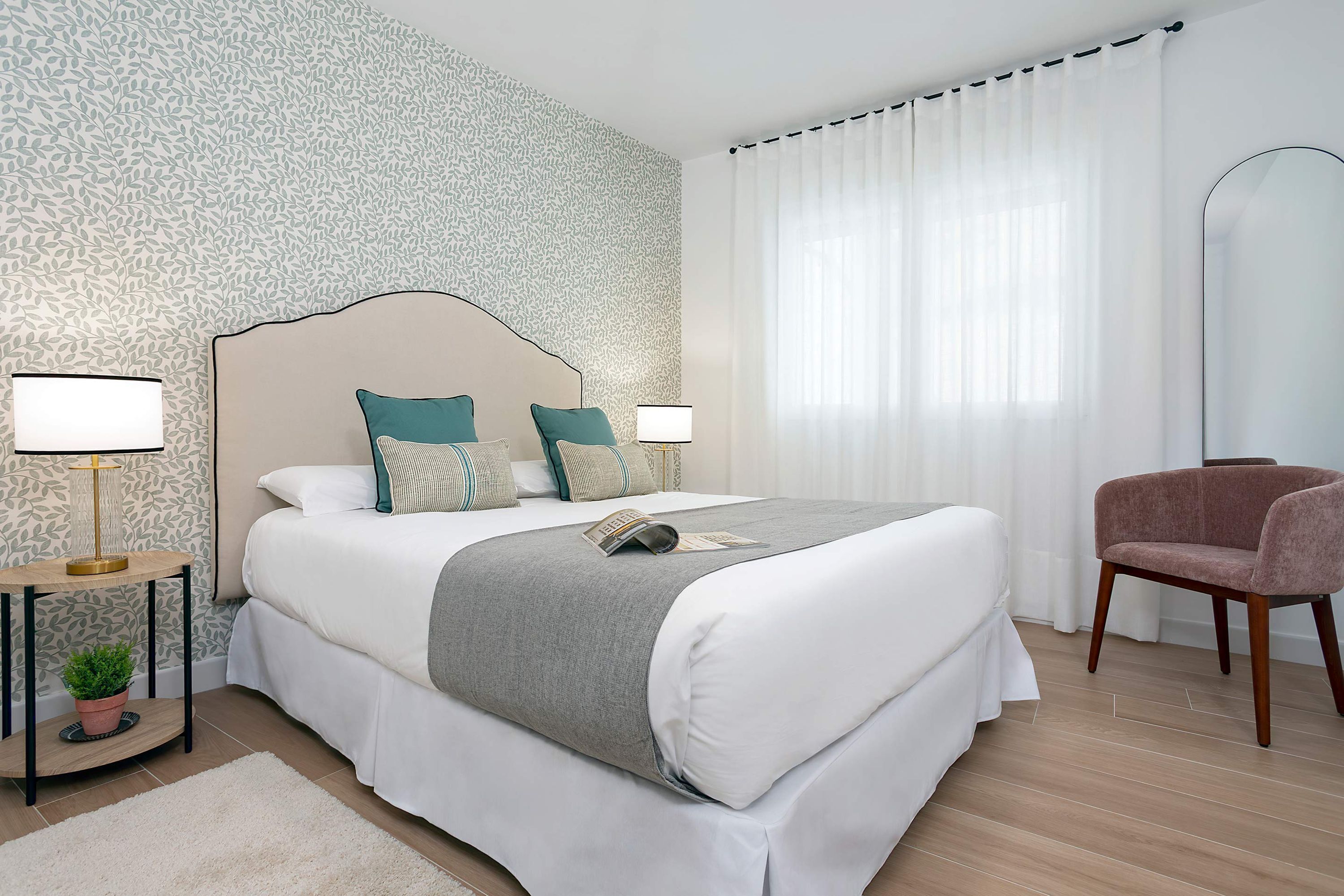 A neatly arranged hotel room with a large bed, two bedside lamps, a chair, and a mirror.