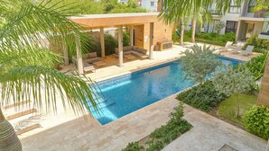 A pool area with a covered seating area, a pool, and surrounding greenery.